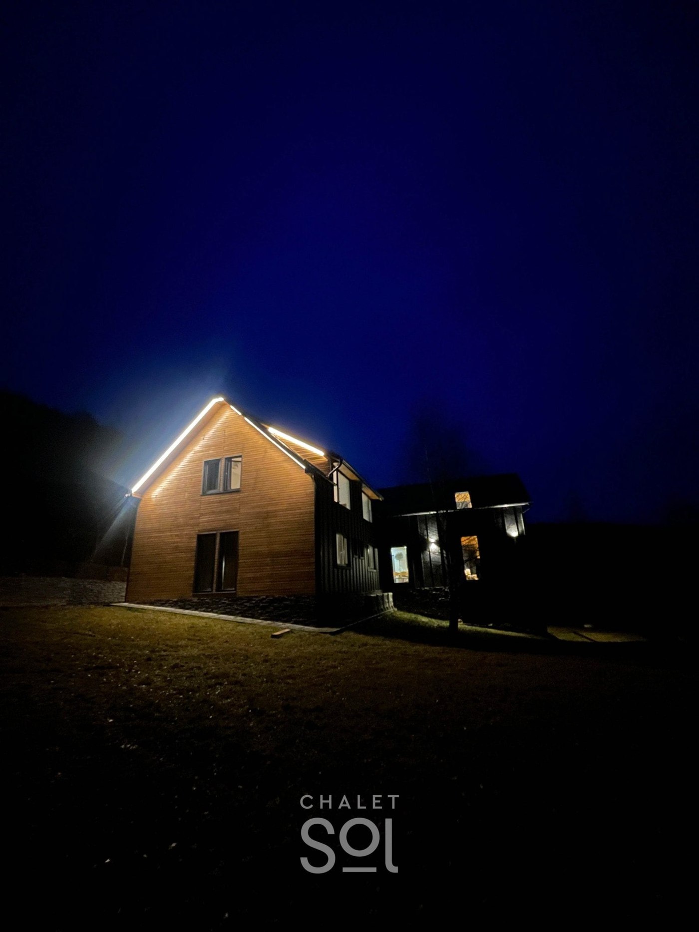 Chalet Sol dopo il tramonto — l'intera casa illuminata contro la valle